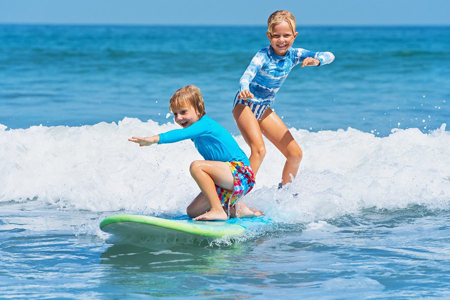 About Our Agency - Happy Boy and Girl are Having Fun Surfing Together on One Board in the Ocean