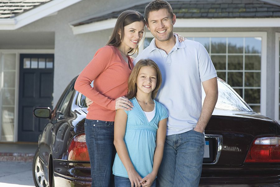 Personal Insurance - Portrait of a Happy Couple With Their Daughter Standing Against Their Car and House